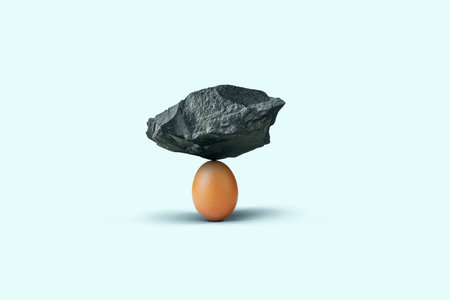 Stone balances on an egg on a blue background. Insurance, concept. Balance and strength, creative idea. Strong creative eggの写真素材
