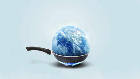 Planet earth burns in a frying pan on a gas burner on a blue background, concept. Global warming and climate change, creative idea. Save planet earthの写真素材