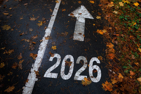 Road marking with the number 2026 and an arrow pointing forward, symbolizing future, progress, and new beginnings. Autumn leaves scattered on the path. New Year 2026, creative idea.の写真素材