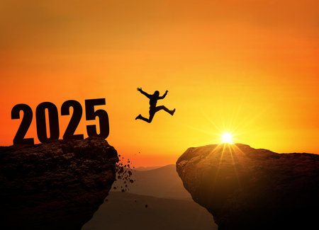 Silhouette of a person jumping across a cliff with the number 2025 at sunset. Concept of new year, challenge, success, goals, future opportunities, and overcoming obstacles.の写真素材