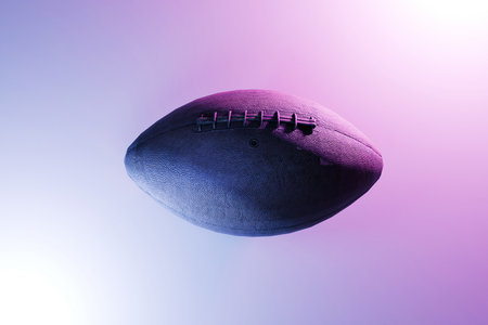 Close-up of an American football isolated on a gradient purple background, symbolizing sport, competition, and athletic lifestyle. Ball with blue and pink lightの写真素材