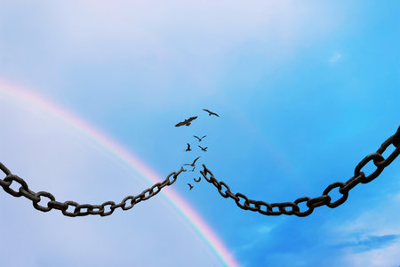 Broken chains against a blue sky with birds flying and a rainbow in the background, symbolizing freedom, hope, liberation, and breaking boundaries. Ideal concept for inspiration and changeの写真素材