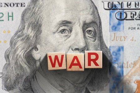 Wooden blocks spelling âWARâ placed on a US dollar bill with Benjamin Franklin's portrait, symbolizing the financial cost of war, economic conflict, or military spending.の写真素材