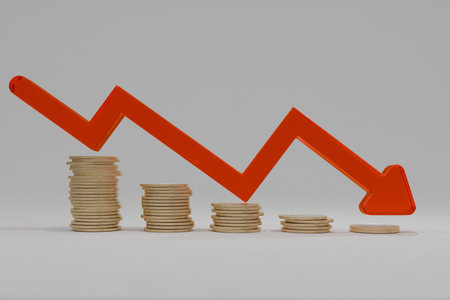 Stacked coins with a red downward arrow symbolizing financial loss, economic crisis, inflation, or recession. Concept of declining savings, investment risk, and market downturn.の写真素材