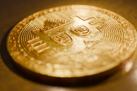Close-up of a shiny golden Bitcoin lying on a reflective surface, symbolizing cryptocurrency,...
