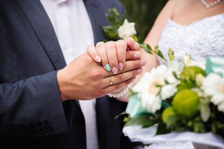 Hands and rings on the background of the costume of the groom and the bride's wedding bouquetの写真素材
