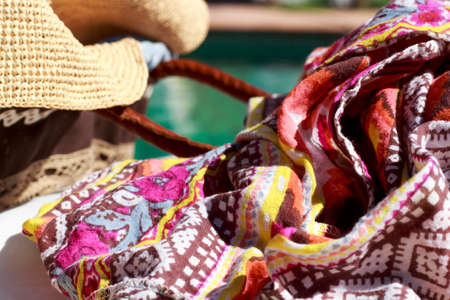 Close-up of sarong beside a sun hat and a beach bag, with a swimming pool in backgroundの写真素材