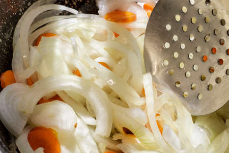 Stirring the sautÃ©e of onion rings and carrot slices with a skimmerの写真素材