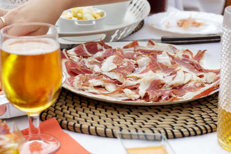 Dish of iberian ham slices beside beer glass and other foodsの写真素材