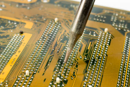 Detail view of soldering iron heating a motherboard component to replace it