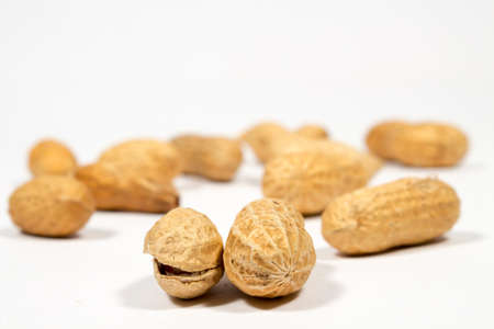 Two peanuts in shell in front of other ones, on white