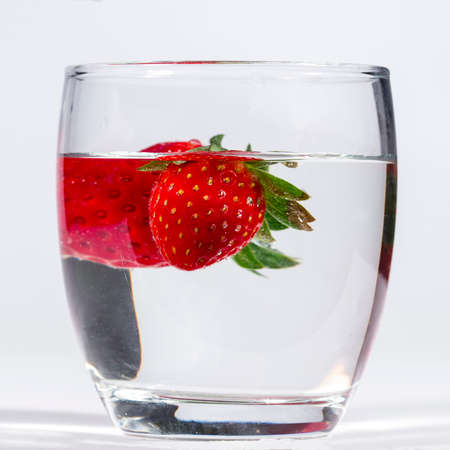 Water glass with several floating strawberriesの写真素材