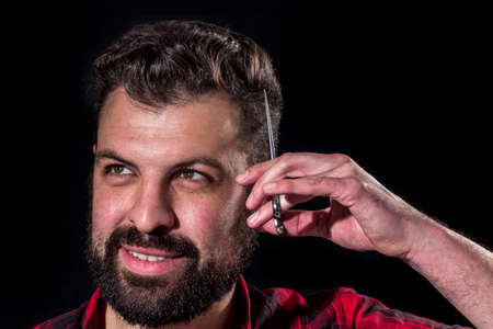 Crazy bearded young scratching his head with scissors