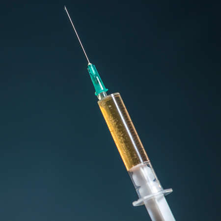 Hypodermic needle and syringe with dark yellow drug, on dark blue background