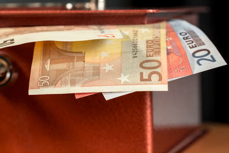 Several euro banknotes sticking out of a metal moneyboxの写真素材