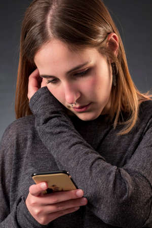 Portrait of young woman with nose ring who is reading a message on her smartphoneの写真素材