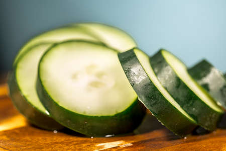 Detail of cucumber slices on wooden floor and blue backgroundの写真素材