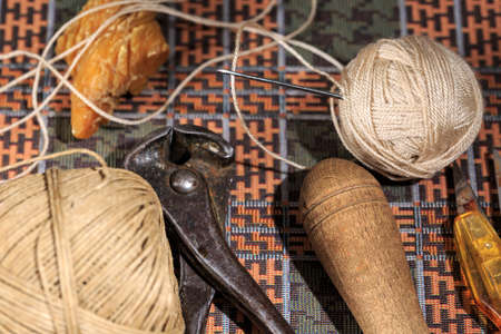 Leather needle beside waxed thread and hand tools used by shoemakers
