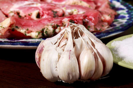 Garlic bulb in front of a dish with raw turkey meat marinated with garlic and parsley, and small dish with saltの写真素材