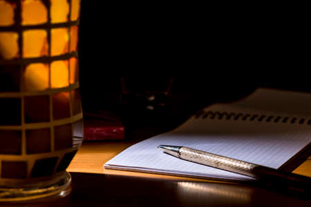 Metal pen over a notebook, beside crystal pencil holder of different colors. Chiaroscuroの写真素材
