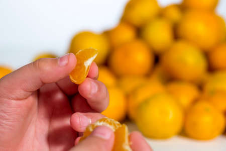 Child has an orange tangerine segment between his fingers. Detail view. Heap of citrus fruits at...