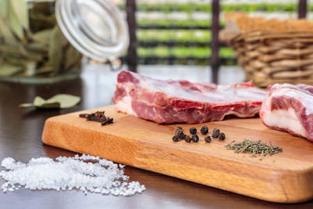 Seasoning raw pork ribs with salt and different spices and hebs. Kitchen board detail with a window at backgroundの写真素材