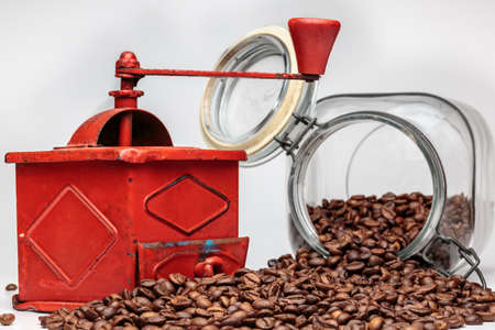 Vintage coffee grinder beside overturned glass jar with coffee beans, on white backgroundの写真素材
