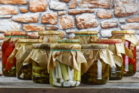 Jars with pickled vegetables arranged in order of bowling pins on wooden shelf against stone wallの写真素材