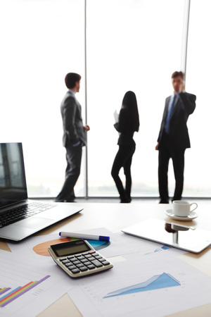 desk with laptop and finance report with business people in backgroundの写真素材