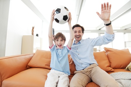 father and son wathcing football inside their houseの写真素材