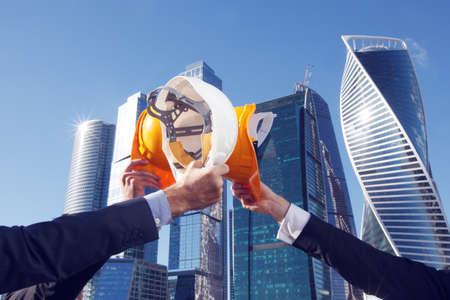 Group of business people clinking their helmets as a success on skyscrapers background, construction finished conceptの写真素材