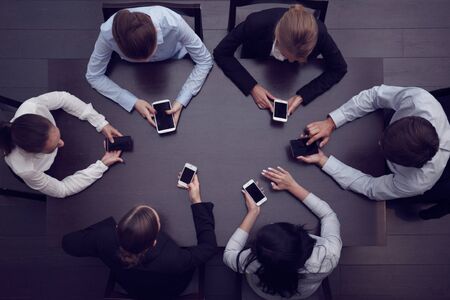 Business people with smartphones sitting around the table, top viewの写真素材
