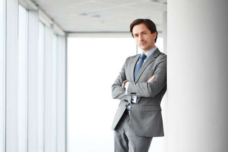 Portrait of handsome businessman standing near windows in officeの写真素材