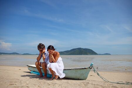 Sad couple sitting on old boat on tropical beachの写真素材