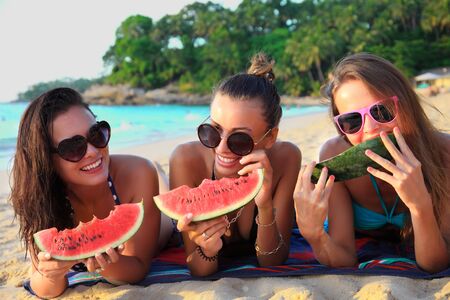 Happy smiling female friends lying on tropical beachの写真素材