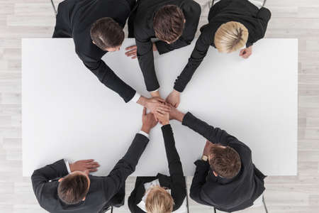 Business team stacking hands sitting around white table