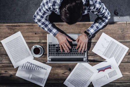 Businessman working on laptop with financial documents, top viewの写真素材
