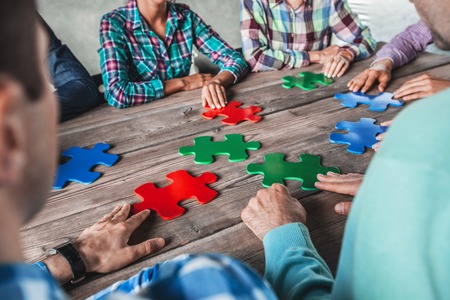 Business people and puzzle on wooden table, teamwork concept
