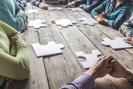 Business people and puzzle on wooden table, teamwork concept
