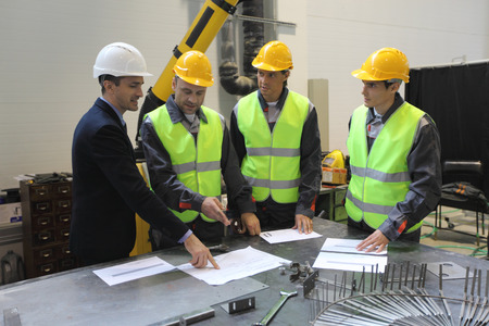 Team of workers and foreman look at documents and blueprints on table at factory