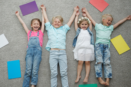 Four happy children laying on floor and smiling among colorful paperの写真素材
