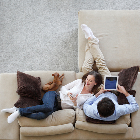 Couple using digital tablet at home sitting on sofa, top viewの写真素材
