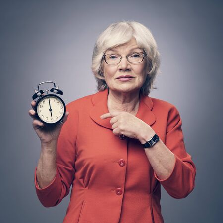 Senior lady pointing to alarm clock showing time of deadlineの写真素材