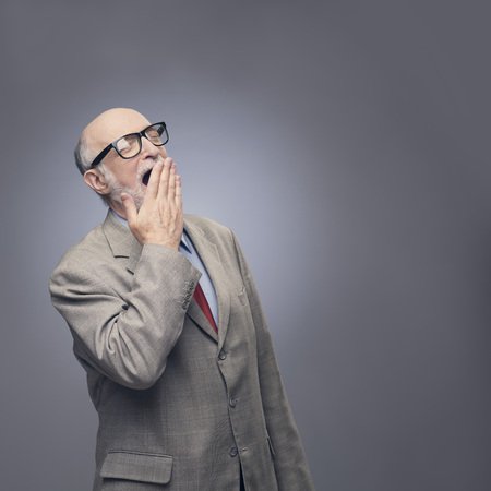 Yawning senior man in suit on gray background with copy spaceの写真素材