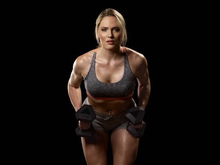 Muscular woman doing exercises with dumbbells for back, isolated on black backgroundの写真素材
