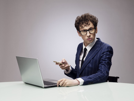 Funny businessman in glasses with laptop and phone, studio shot on gray backgroundの写真素材