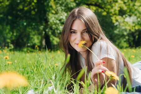 Beautiful young woman laying on grass with dandelion flowers in parkの写真素材