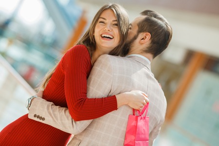 Happy beautiful young couple with gift bag hug in shopping mallの写真素材