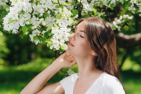 Beautiful young brunette woman standing near blooming apple treeの写真素材