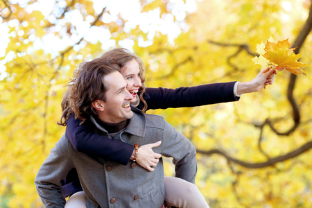 Love, relationships, season and people concept - happy young couple having fun in autumn park piggyback rideの写真素材